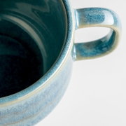 Detailaufnahme einer blau glasierten Keramik-Tasse mit Henkel, schräg von oben/seitlich vor weißem Hintergrund