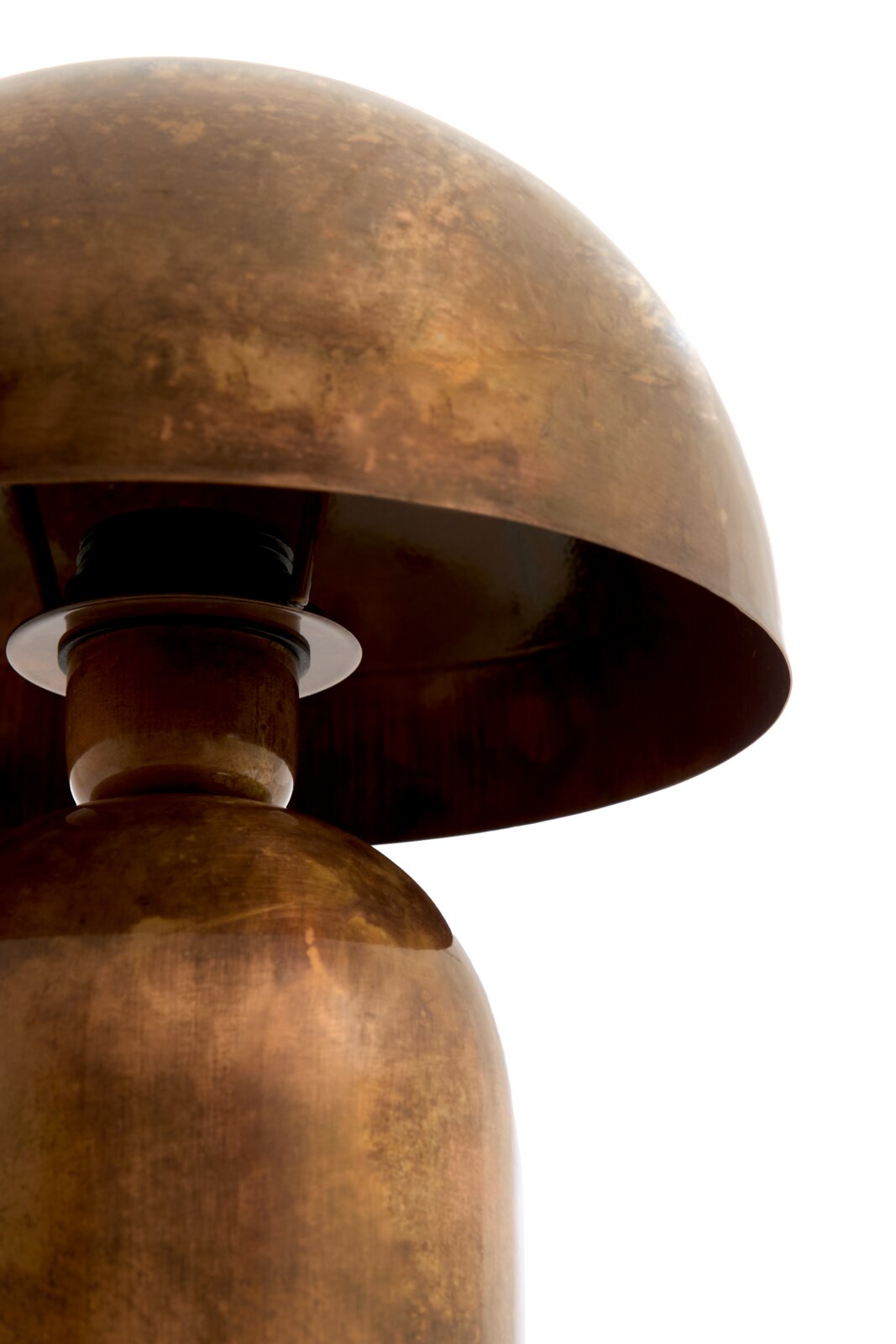 Detailopname vanuit laag zijaanzicht van een sculpturale tafellamp met afgeronde voet en koepelvormige kap in warm, verweerd messing.