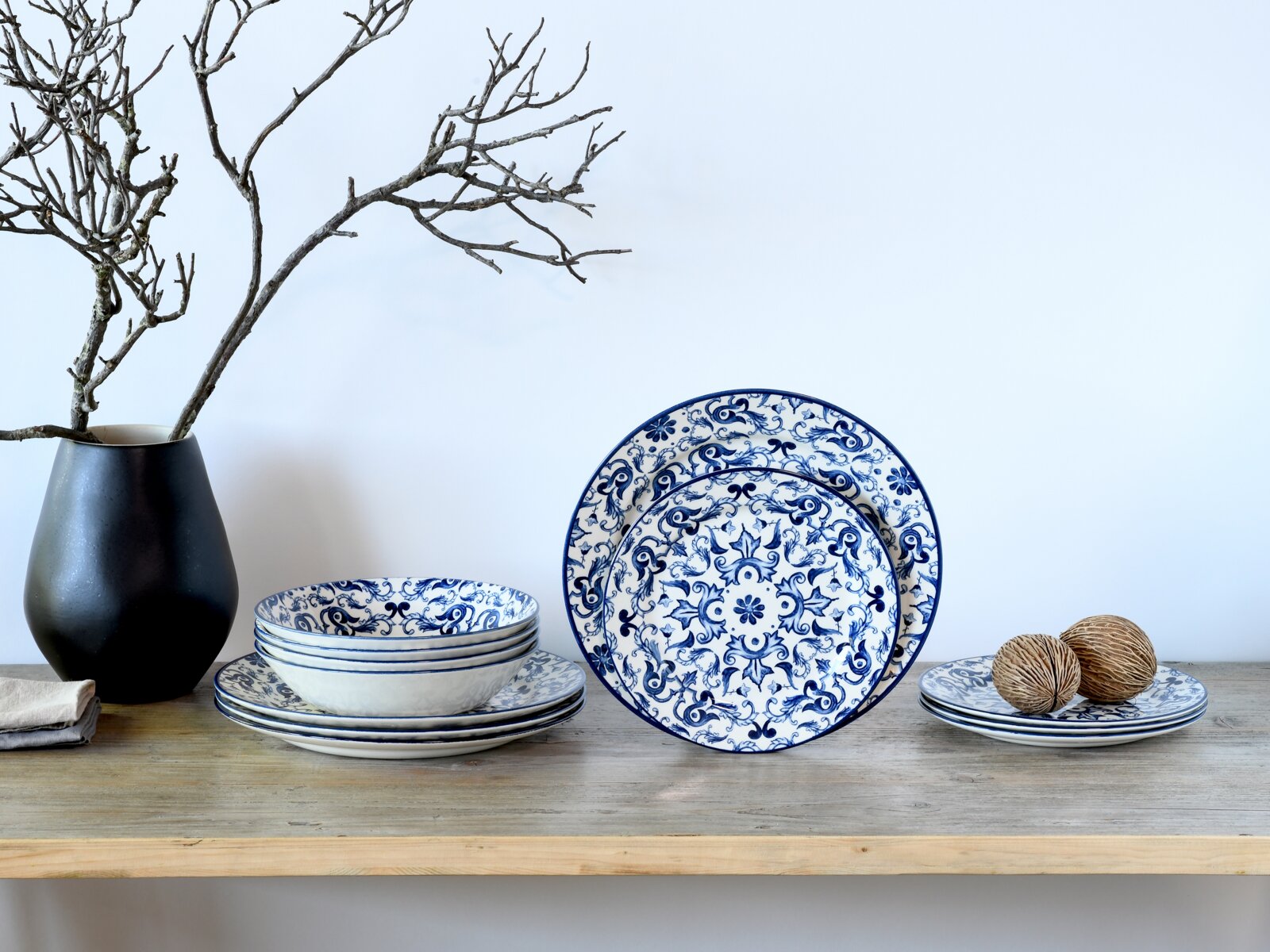 Blau-weiß gemustertes Keramik-Geschirrset mit Tellern und Schalen im Ornamentdesign auf Holzablage vor hellem Hintergrund, frontal in leicht erhöhter Perspektive