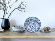 Blau-weiß gemustertes Keramik-Geschirrset mit Tellern und Schalen im Ornamentdesign auf Holzablage vor hellem Hintergrund, frontal in leicht erhöhter Perspektive