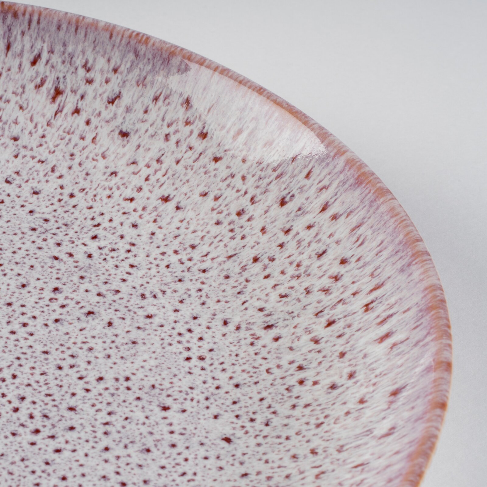 Nahaufnahme einer gesprenkelten Keramikschale in Weiß mit rötlich-braunen Sprenkeln und roséfarbenem Rand, aufgenommen in schräger Draufsicht vor hellem Hintergrund