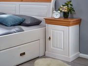 Nachtkonsole 1-türig aus Holz mit weißem Korpus und naturfarbener Oberseite, seitliche Perspektive, dekoriert mit einer Uhr und Blumen.