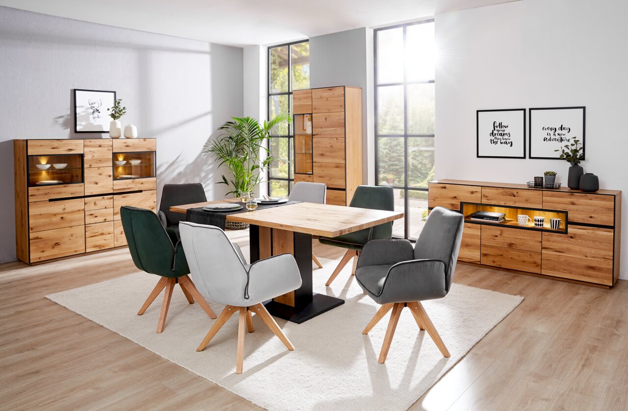 Linea Natura Sideboard mit Beleuchtung KELIO Esszimmer mit modernem Esstisch aus Holz und Metall, umgeben von gepolsterten Stühlen in verschiedenen Farben. Im Hintergrund sind Vitrinen und Sideboards aus Holz mit Beleuchtung zu sehen. Perspektive: Frontalansicht des Esszimmers.