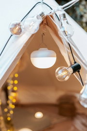Nahaufnahme von oben auf den Zelteingang: eine runde, weiße Campinglampe hängt im Inneren, umgeben von einer Lichterkette mit Glühbirnen.