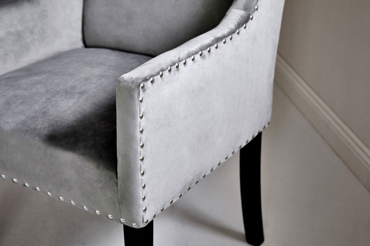 Nahaufnahme eines grauen Stuhls mit Nietenverzierung und schwarzen Beinen, seitliche Perspektive.