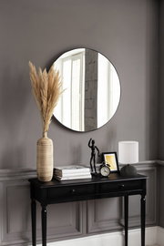 Runder Spiegel mit einem Durchmesser von ca. 50 cm, an einer grauen Wand über einem schwarzen Konsolentisch mit Dekorationen wie einer Vase mit Pampasgras, einer Tischlampe und einem Wecker. Perspektive: Frontalansicht.