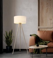 Beige Dreibein-Stehlampe mit zylindrischem Stoffschirm in Wohnzimmerecke neben braunem Sofa und kleinem Beistelltisch, Frontansicht auf Augenhöhe