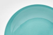Nahaufnahme eines türkisfarbenen Tellers mit feinen konzentrischen Kreisen, von oben betrachtet.