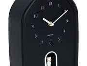 Schwarze Wanduhr mit weißen Ziffern und Zeigern, rechteckige Form mit abgerundeten Ecken, kleine weiße Katze in einer Öffnung unten, seitliche Perspektive.