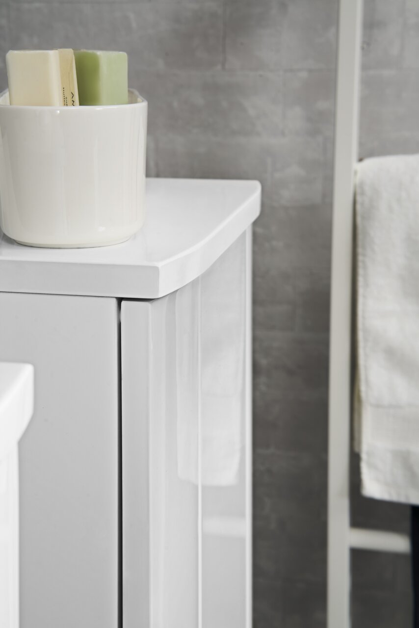 Nahaufnahme eines weißen Midischranks mit glänzender Oberfläche, auf dem ein weißer Behälter mit Seifenstücken steht. Perspektive von der Seite.