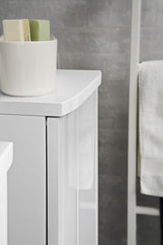 Nahaufnahme eines weißen Midischranks mit glänzender Oberfläche, auf dem ein weißer Behälter mit Seifenstücken steht. Perspektive von der Seite.