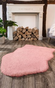 Rosa Lammfell Teppich vor einem Kamin mit Holzstapeln, aus der Perspektive des Bodens aufgenommen.