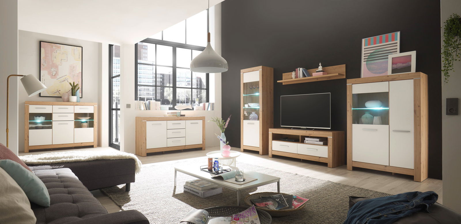 Moderne Wohnwand und Sideboards in einem hellen Wohnzimmer mit großen Fenstern, aus hellem Holz und weißen Fronten, aus der Perspektive des Wohnzimmers fotografiert.