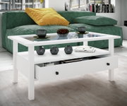 Weißer Couchtisch mit Glasplatte, offener Ablage und halb geöffneter Schublade im modernen Wohnzimmer vor grünem Sofa, Perspektive: frontale leicht schräge Ansicht von vorne links