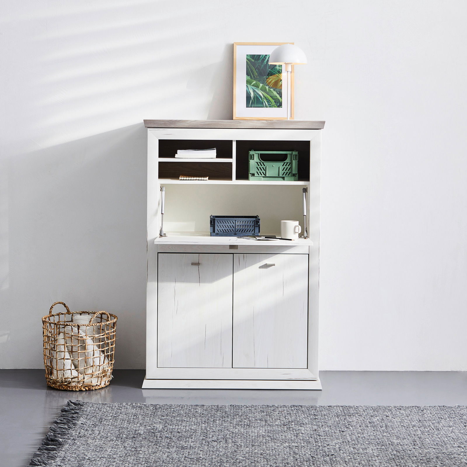 Weißer Sekretär mit Klapptür, Regalfächern und Schranktüren, frontal fotografiert. Dekoriert mit Lampe und Bild auf der Oberseite.