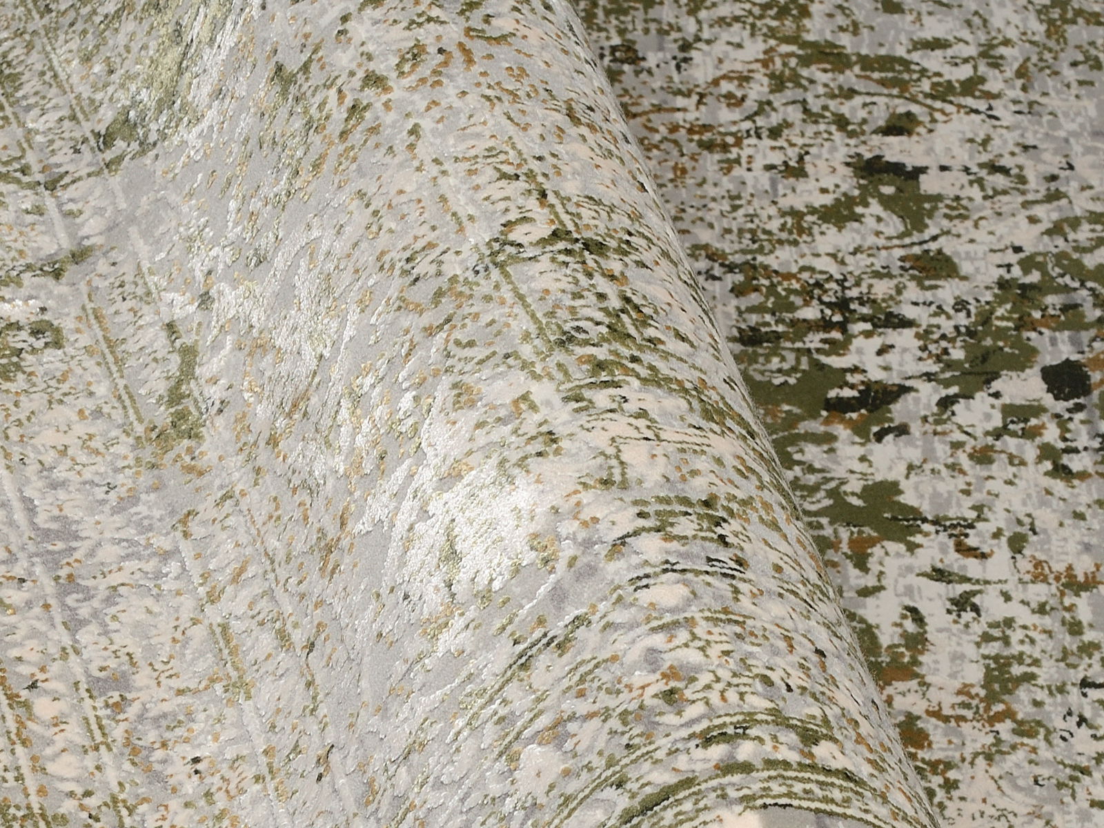 Designer Teppich in Nahaufnahme, mit einem modernen, abstrakten Muster in Grün- und Grautönen. Der Teppich ist teilweise aufgerollt, was die Textur und das Design aus einer seitlichen Perspektive zeigt.