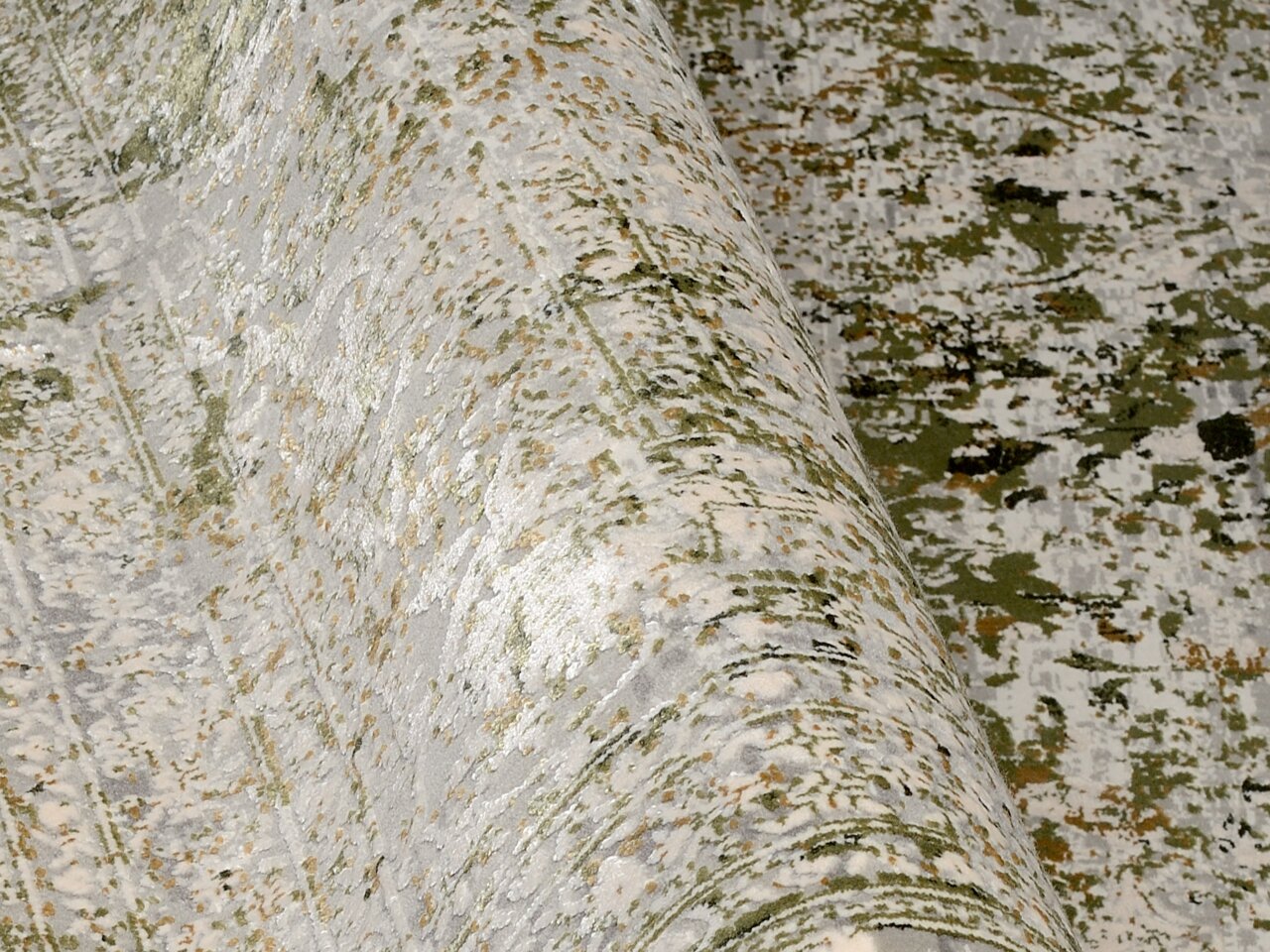 Designer Teppich in Nahaufnahme, mit einem modernen, abstrakten Muster in Grün- und Grautönen. Der Teppich ist teilweise aufgerollt, was die Textur und das Design aus einer seitlichen Perspektive zeigt.