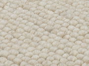 Nahaufnahme eines handgewebten Teppichs mit grober, strukturierter Oberfläche in cremeweißer Farbe.