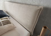 Nahaufnahme eines Massivholzbettes mit einem gepolsterten, gerippten Kopfteil in Beige, seitliche Perspektive.