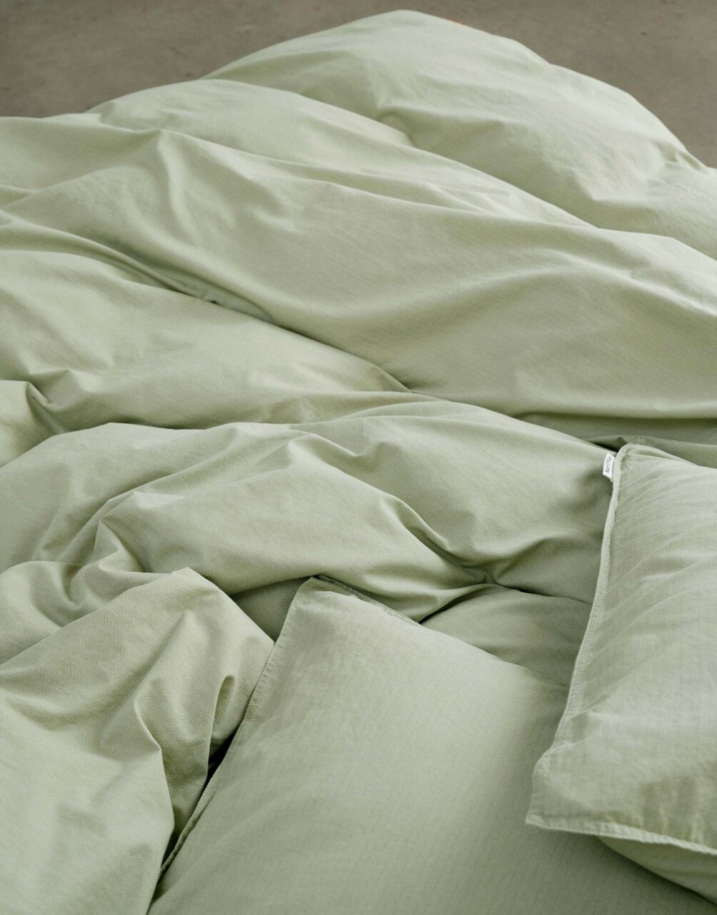 Nahaufnahme von grüner Bettwäsche in 155x220cm Größe, die auf einem Bett liegt.