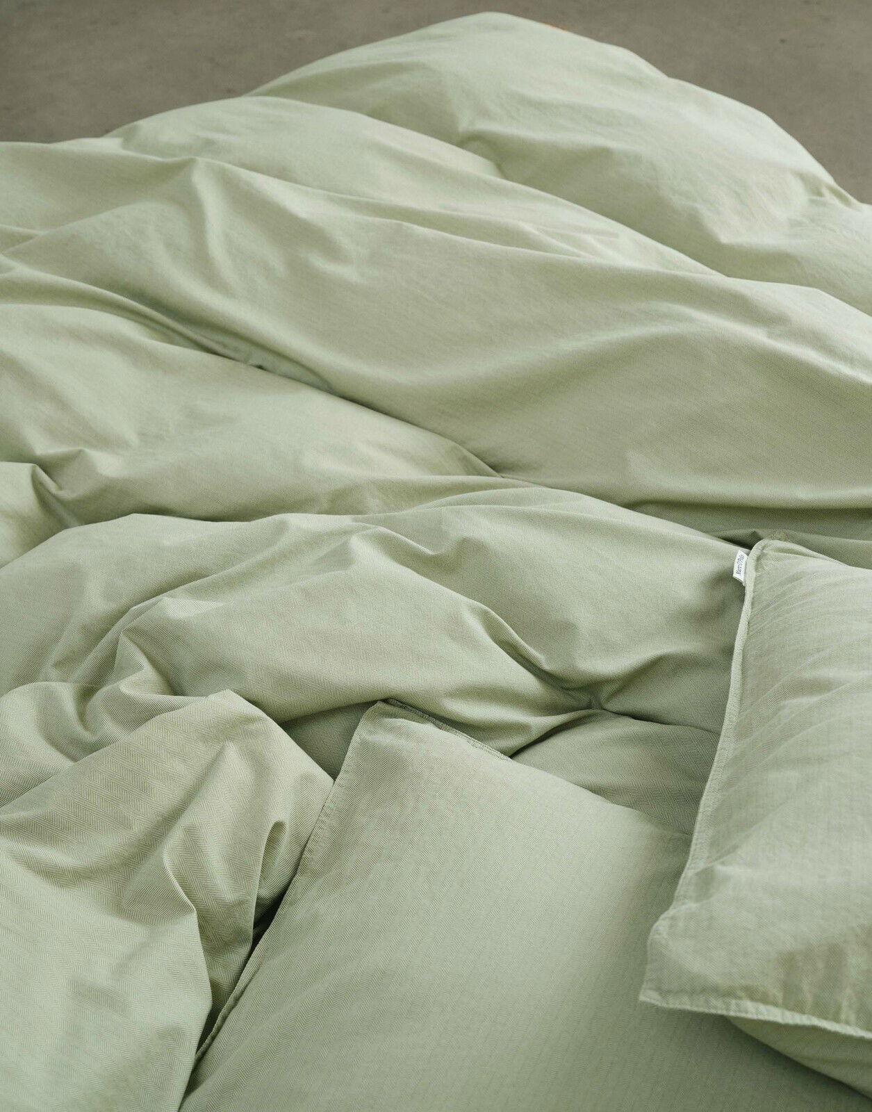 Nahaufnahme von grüner Bettwäsche in 155x220cm Größe, die auf einem Bett liegt.