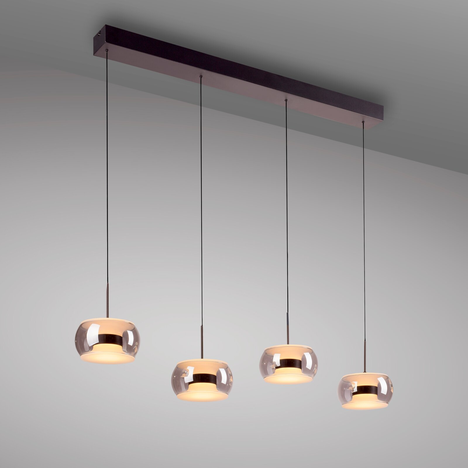 Paul Neuhaus LED-Hängeleuchte FUMEA Moderne 4-flammige Pendelleuchte mit länglicher schwarzer Deckenleiste und vier rauchgrauen Glas-Schirmen, warm leuchtend, perspektivisch von schräg unten (Untersicht) vor hellem Hintergrund