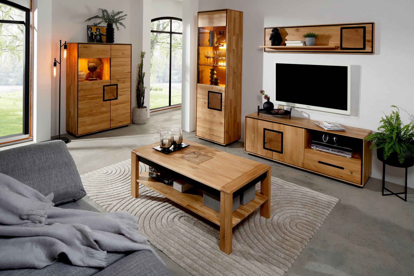 Moderne woonkamerset van massief hout met verlichte vitrinekast, dressoir/tv-meubel, wandrek en salontafel op een licht tapijt, gefotografeerd in een schuin vooraanzicht (licht perspectief van links).