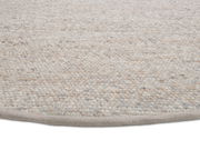 Nahaufnahme eines handgewebten Teppichs mit einer strukturierten, natürlichen Farbpalette. Der Teppich ist aus einer seitlichen Perspektive fotografiert.