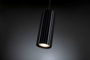 Schwarze, zylindrische LED-Pendelleuchte mit geriffeltem Lampenschirm und warmweiß leuchtendem Spot, schräg von unten im 3/4-Winkel vor dunklem Hintergrund