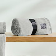 Graue, gerollte Kuscheldecke von s.Oliver auf einem Holztisch, seitliche Perspektive.