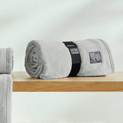 Graue, gerollte Kuscheldecke von s.Oliver auf einem Holztisch, seitliche Perspektive.