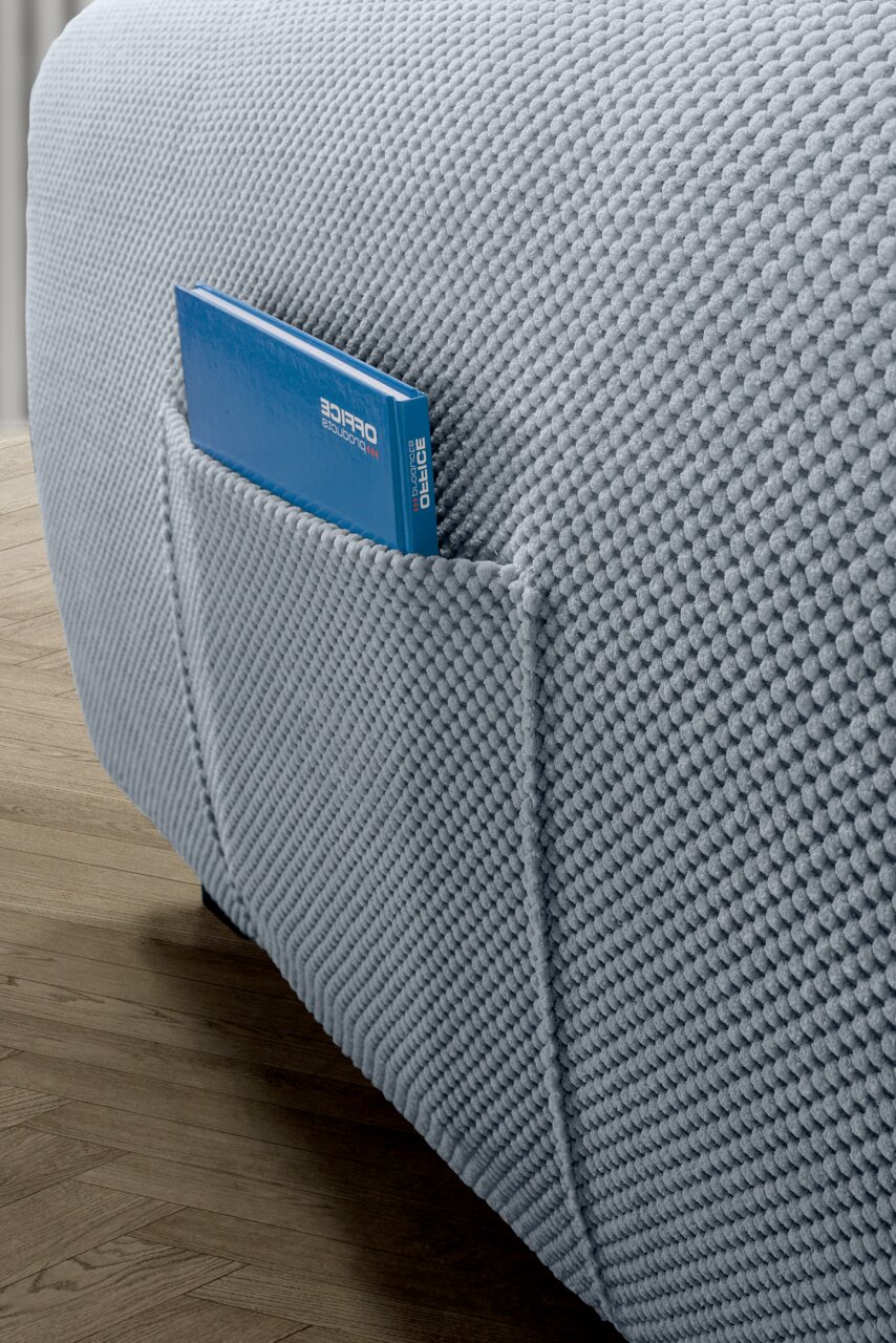 Nahaufnahme einer grauen Rundecke mit strukturierter Oberfläche und einer Seitentasche, in der ein blaues Buch steckt. Perspektive von der Seite.