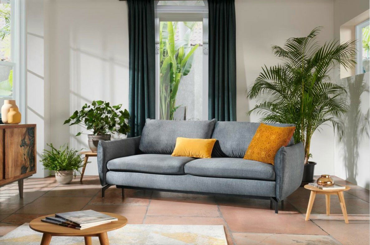 Graues Funktionssofa mit gelben Kissen in einem modern eingerichteten Wohnzimmer, frontal betrachtet.