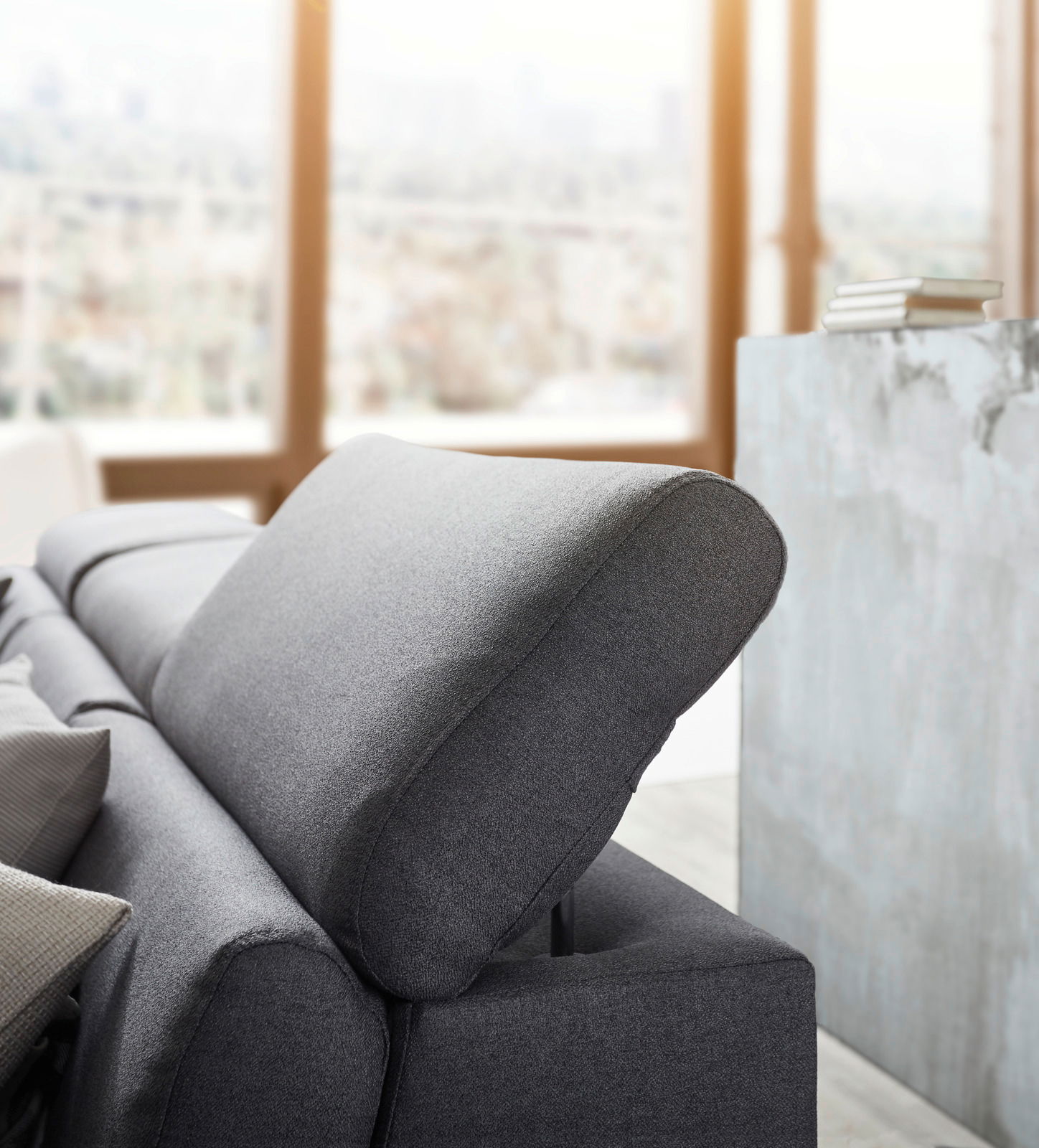 Graues Sofa mit verstellbarer Kopfstütze, seitliche Perspektive in einem modernen Wohnzimmer.