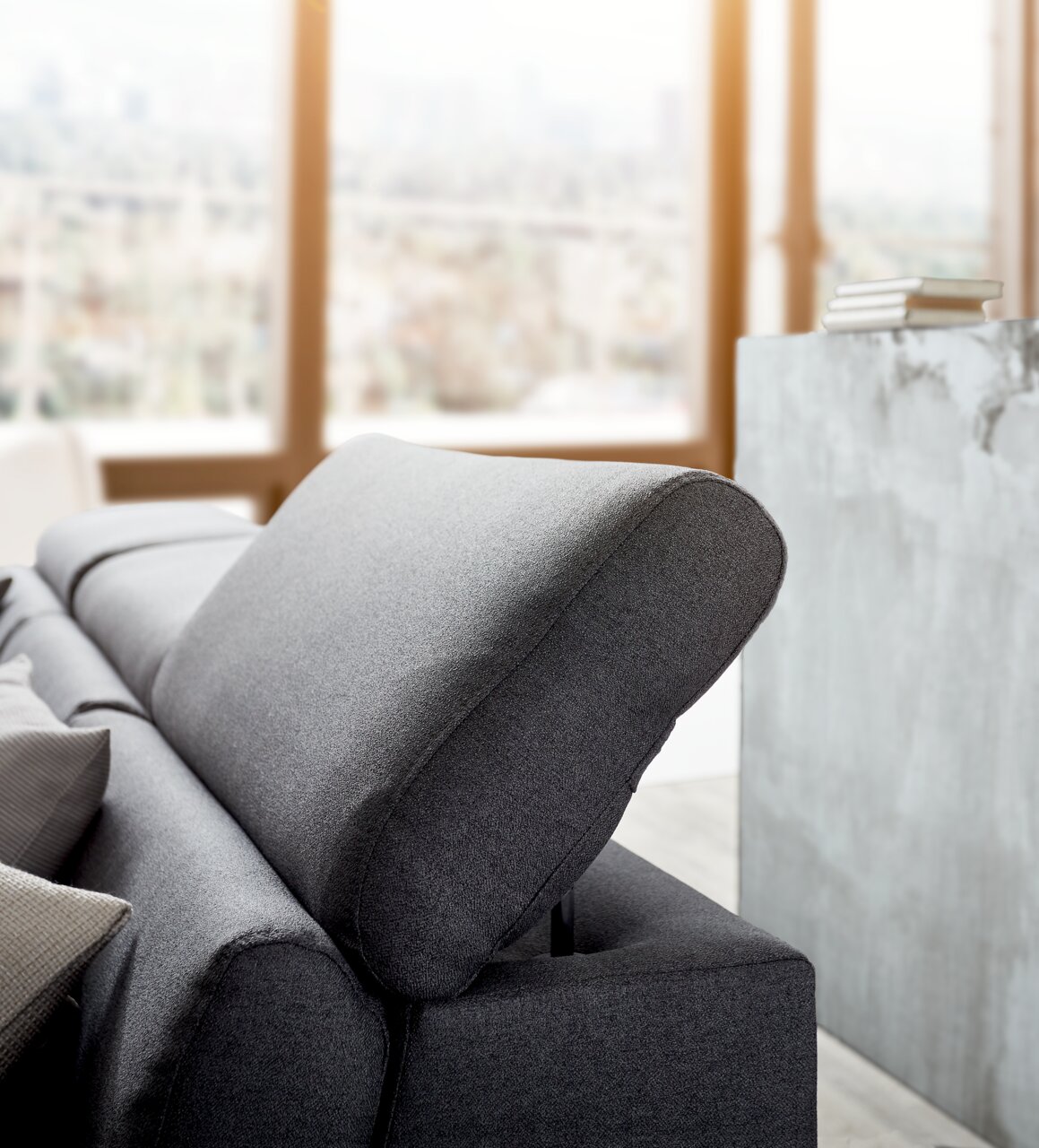 Graues Sofa mit verstellbarer Kopfstütze, seitliche Perspektive in einem modernen Wohnzimmer.