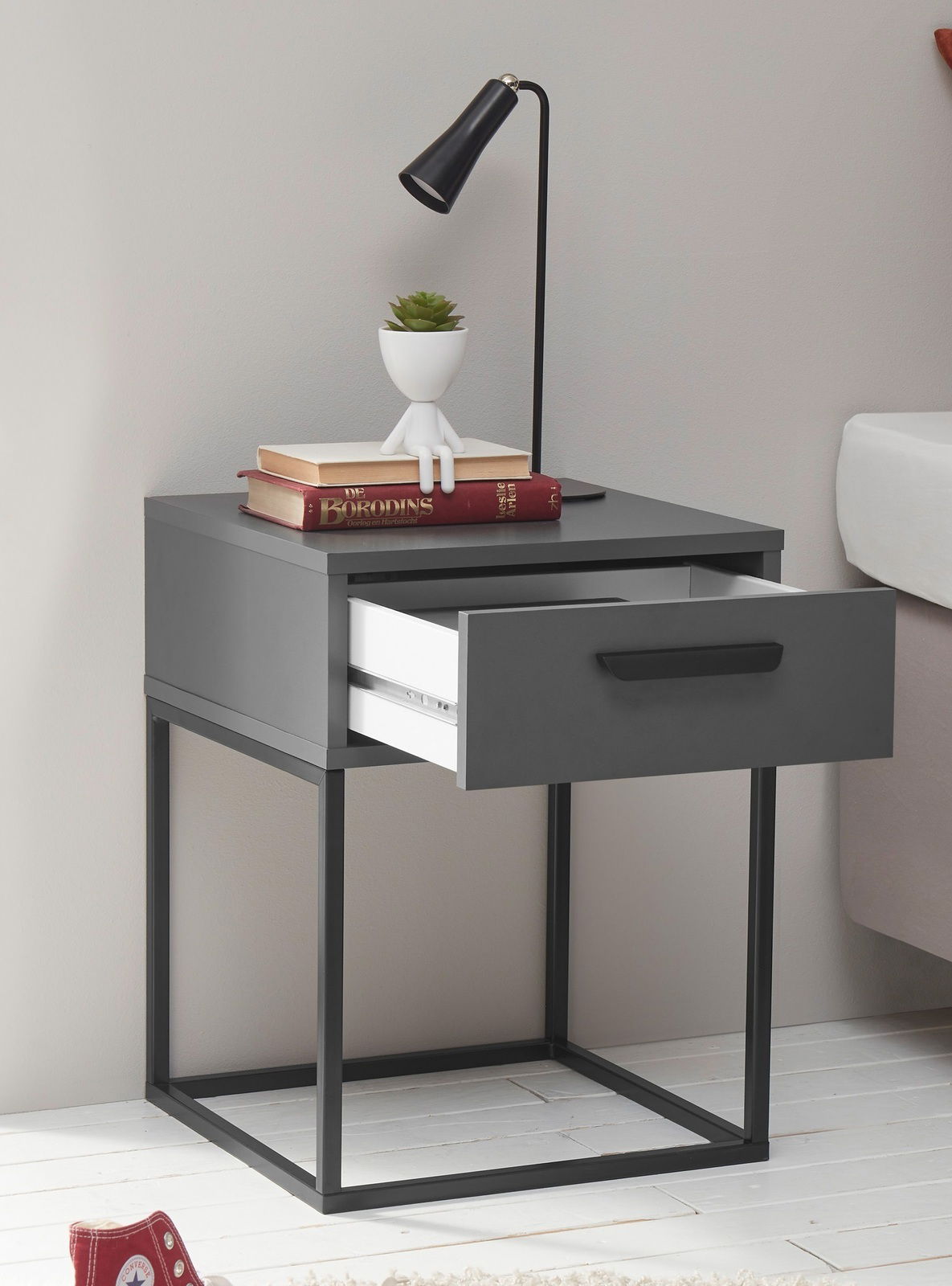 Moderne Nachtkommode mit offenem Schubfach, dekoriert mit Büchern, einer Pflanze und einer Lampe, seitliche Perspektive