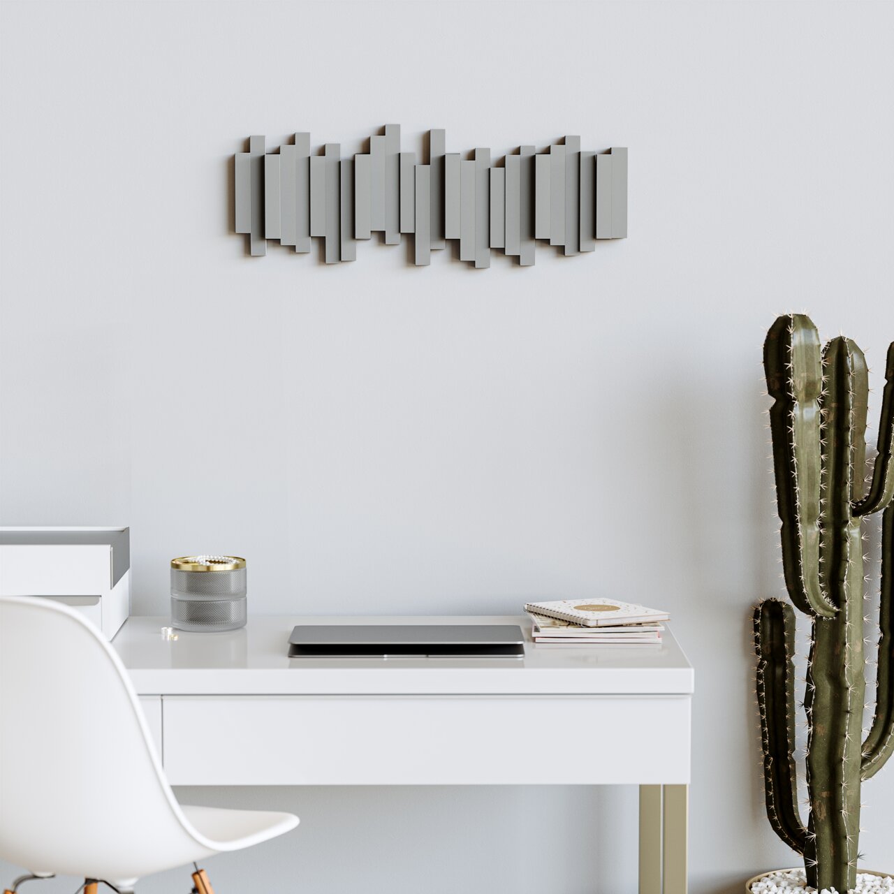 Moderne wandkapstok met een geometrisch ontwerp, aan een lichte muur boven een bureau, met decoraties en een cactus op de voorgrond.