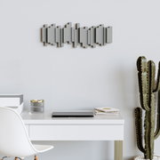 Moderne wandkapstok met een geometrisch ontwerp, aan een lichte muur boven een bureau, met decoraties en een cactus op de voorgrond.