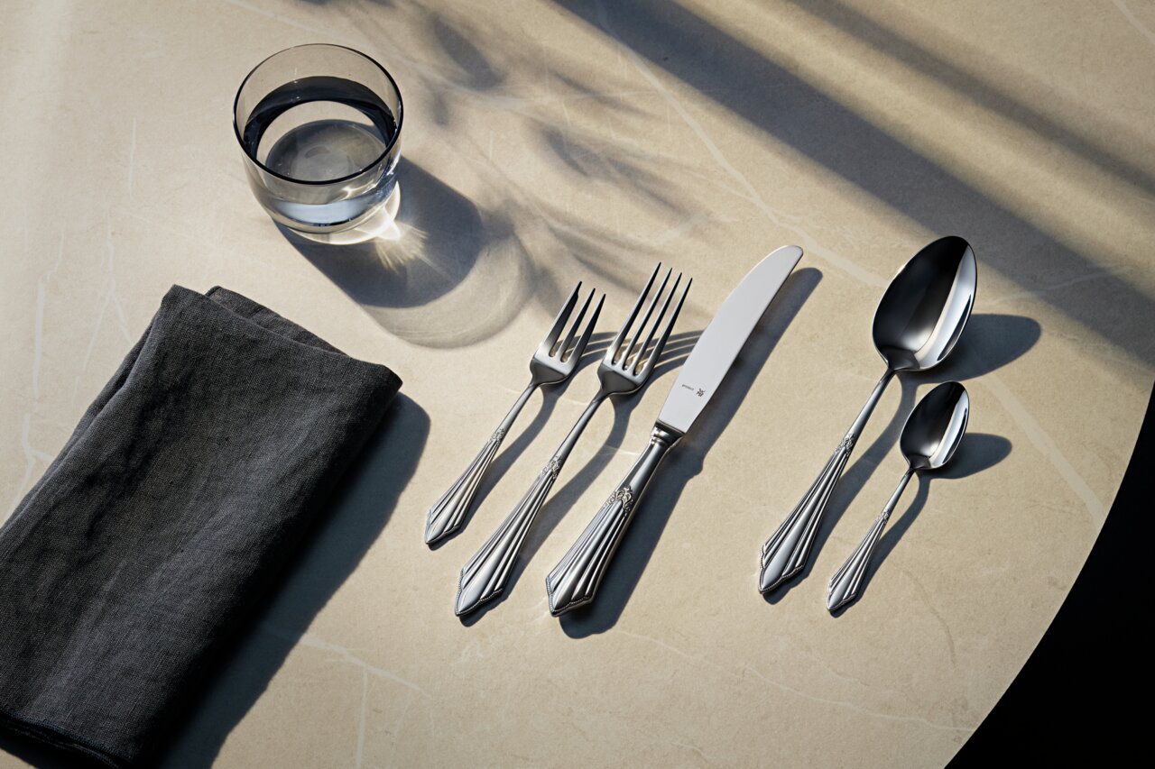 Elegantes Besteckset mit Gabeln, Messer und Löffeln auf einem Tisch, seitliche Perspektive.
