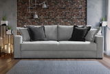 Graues Querschläfer-Sofa mit schwarzen Kissen, frontal vor einer Ziegelwand fotografiert.