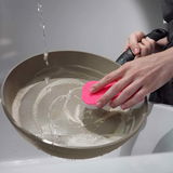 Pfanne 20cm Ceratal Comfort wird von Hand mit einem rosa Schwamm gereinigt, Wasser fließt in die Pfanne, Ansicht von oben.