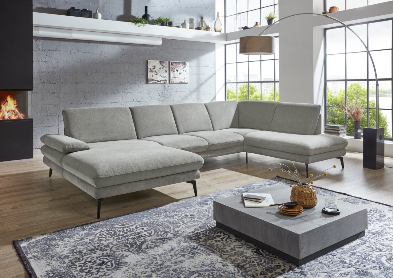 Moderne graue Polsterrundecke in einem stilvollen Wohnzimmer mit großen Fenstern und einem Kamin, seitliche Perspektive.