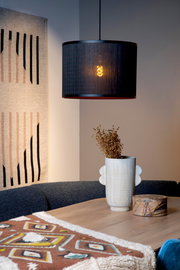 Moderne Pendelleuchte in schwarzem Design, beleuchtet, über einem Esstisch mit Dekorationen, seitliche Perspektive.