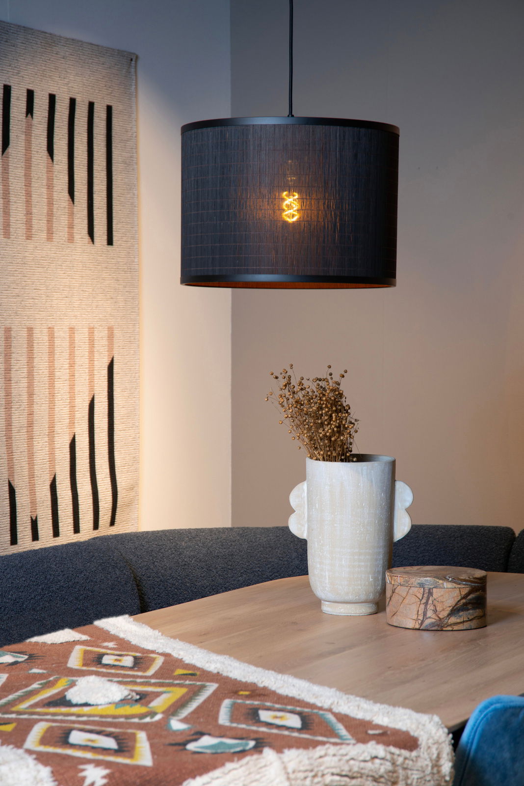 Moderne Pendelleuchte in schwarzem Design, beleuchtet, über einem Esstisch mit Dekorationen, seitliche Perspektive.