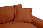 Nahaufnahme eines Big-Sofas in warmem Terrakotta-Ton mit geripptem Stoffbezug und passendem Kissen, seitliche Perspektive.