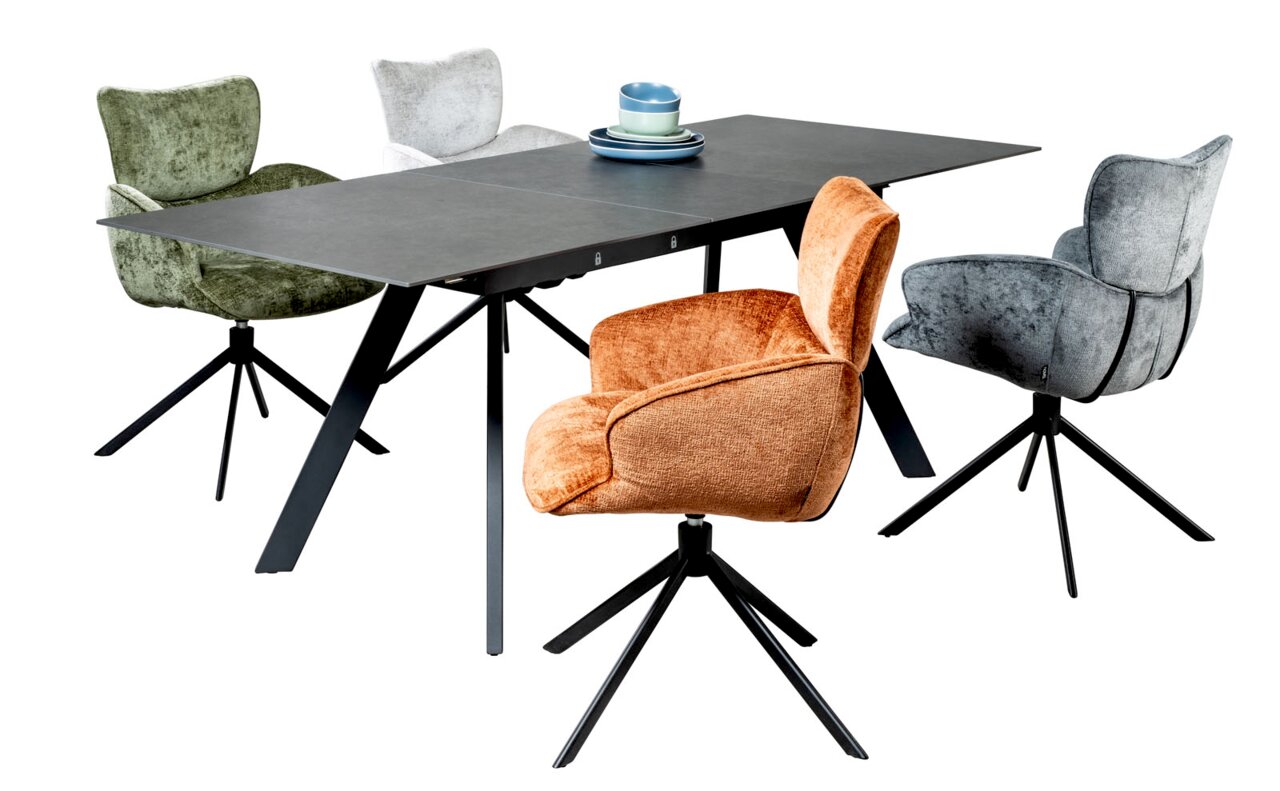 Moderne eettafel met vier gekleurde stoelen met armleuningen, gefotografeerd vanuit een diagonaal perspectief.
