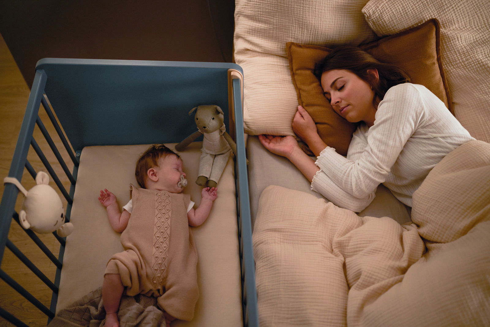 Anstellbett neben einem Bett, in dem ein Baby und eine Frau schlafen, aus der Vogelperspektive.