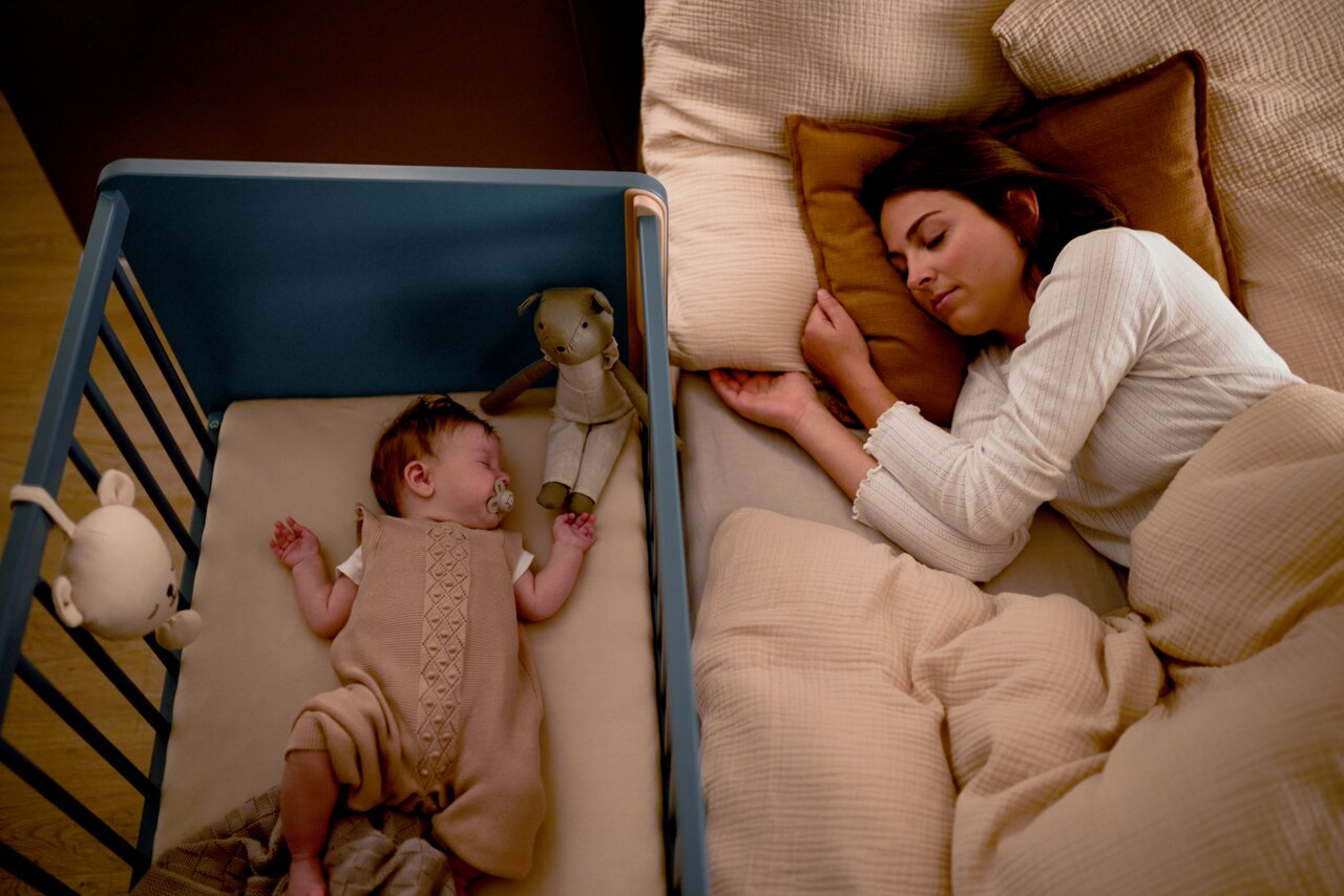 Een opklapbed naast een bed waarin een baby en een vrouw slapen, gezien vanuit vogelperspectief.