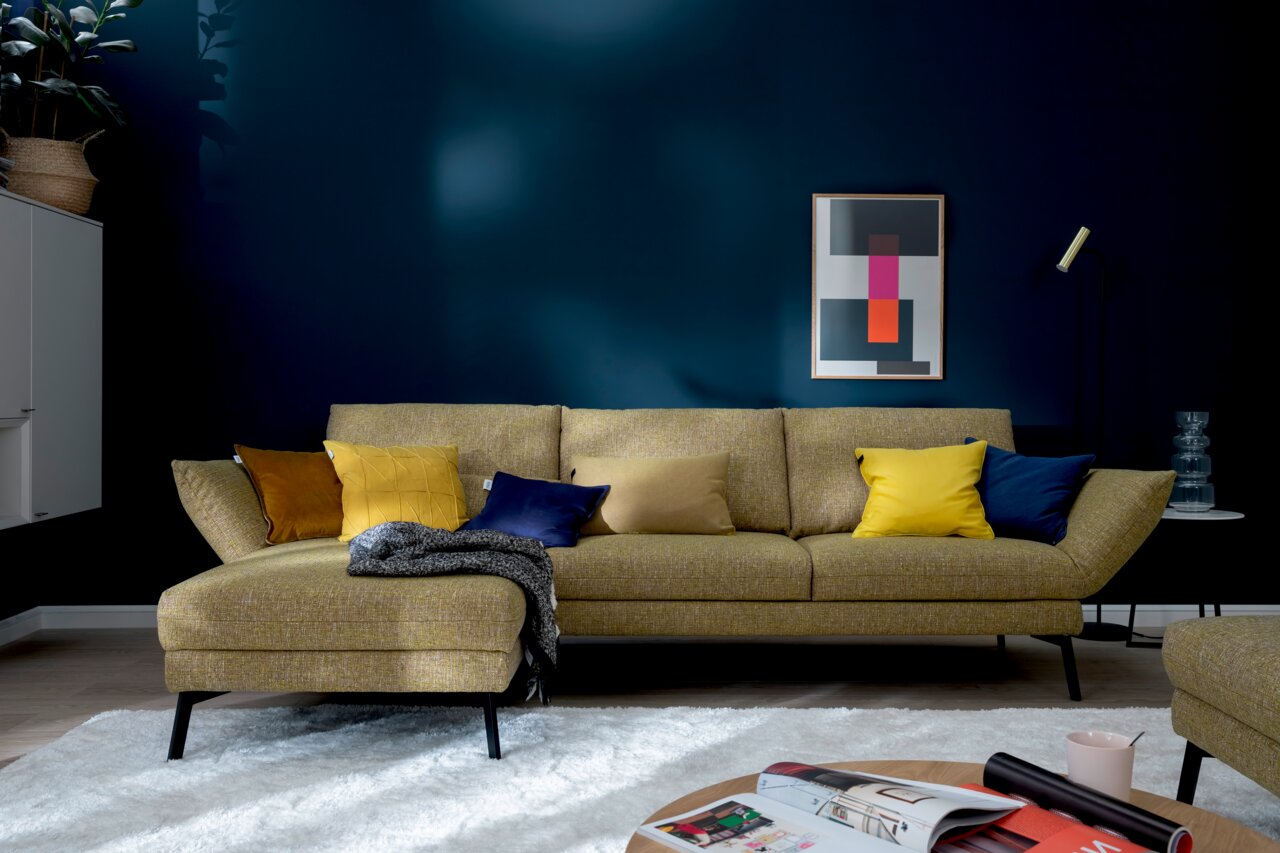 Moderne Longchairkombination in senfgelber Farbe mit bunten Kissen, frontal fotografiert in einem stilvoll eingerichteten Wohnzimmer.