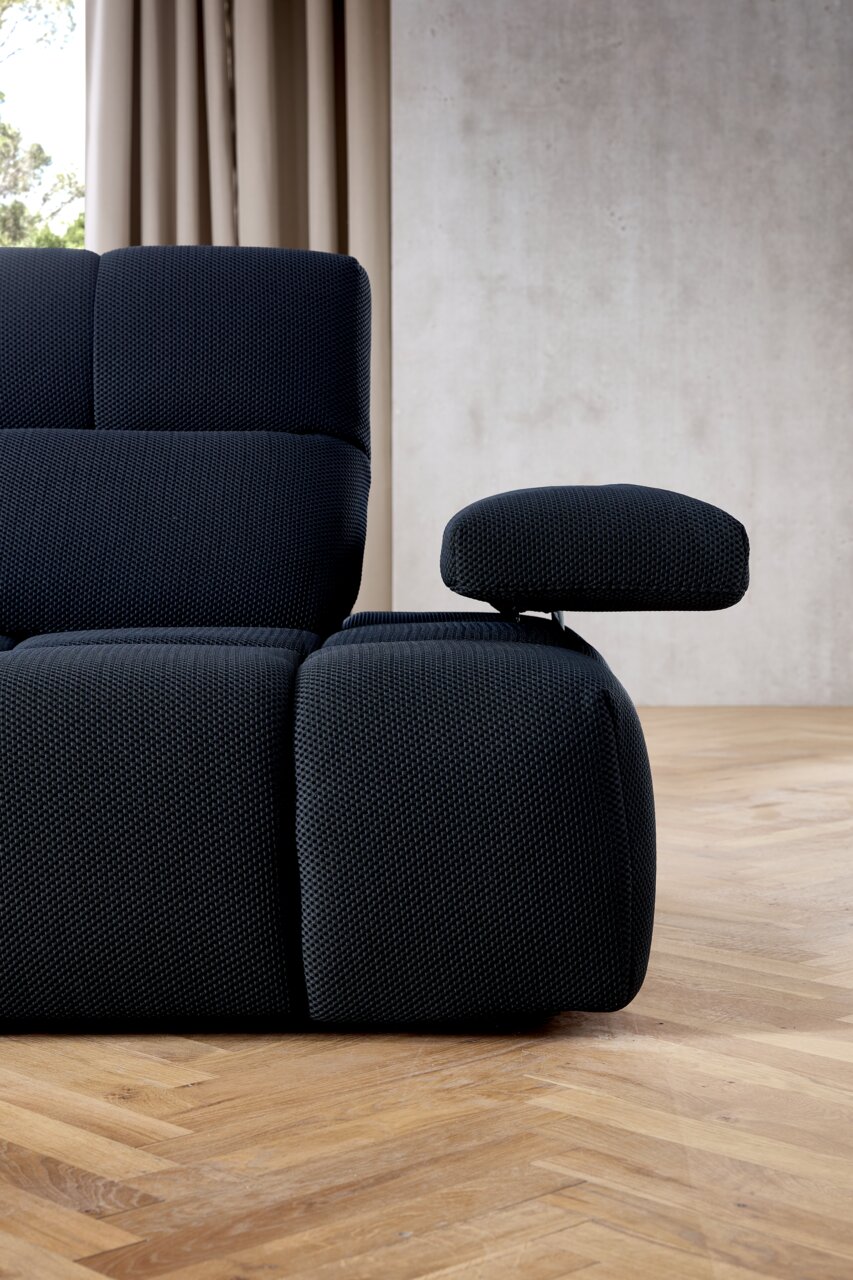 Nahaufnahme einer modernen, dunkelblauen Eckgarnitur mit verstellbarer Armlehne, seitliche Perspektive